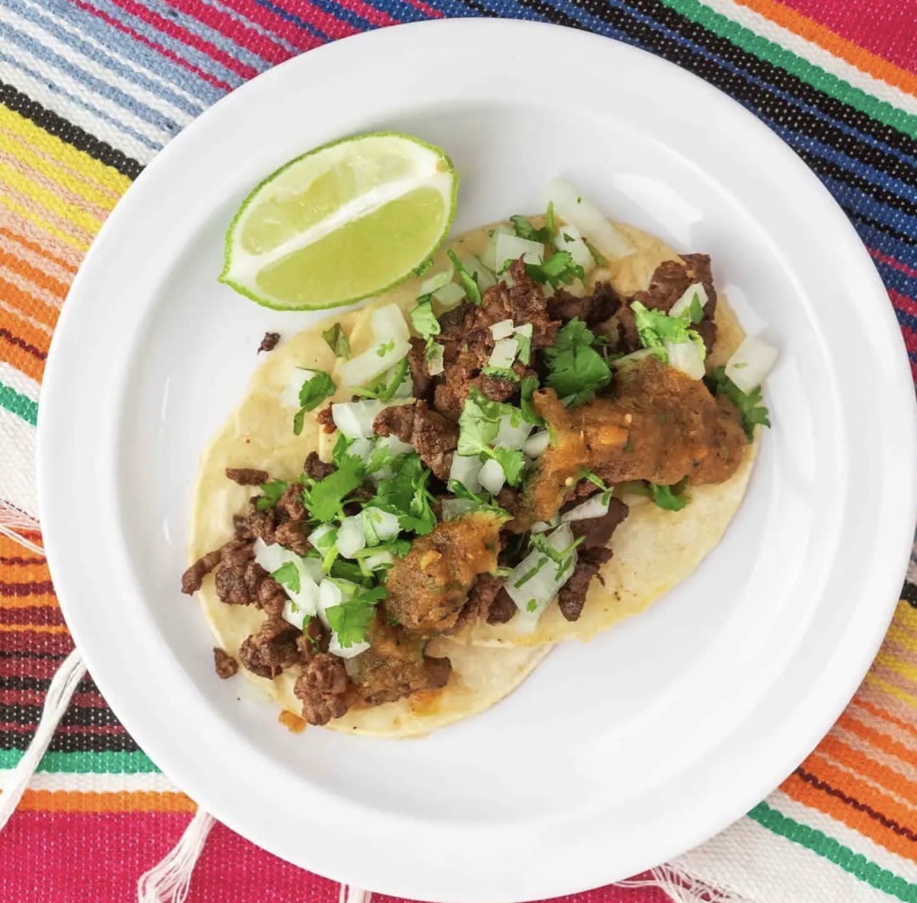 Classic al pastor taco with cilantro, onion, salsa and lime on a colorful Mexican serape